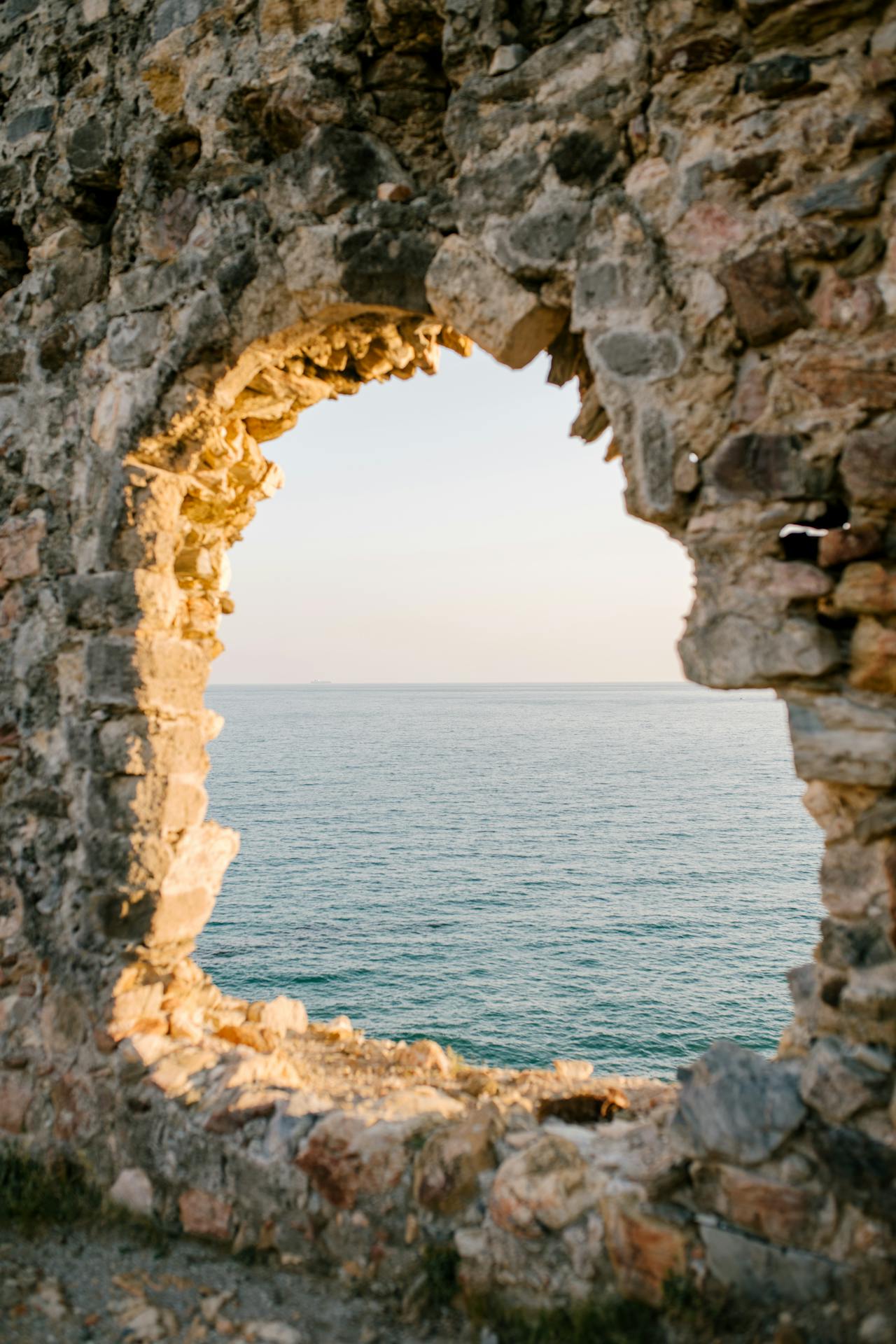 Vue sur la mer à travers une ouverture dans un mur de pierre, symbole de passage de la dualité à la présence et à l’unité.